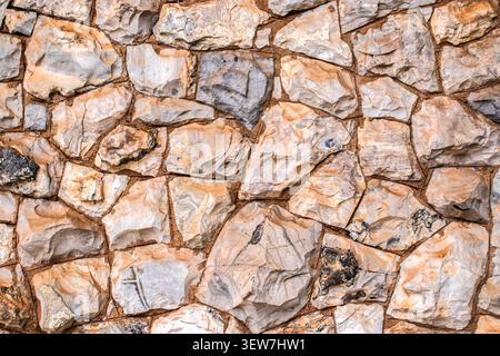 Eine Nahaufnahme der Hintergrundstruktur einer organischen und rustikalen Steinmauer mit unregelmäßigen Felsen, mit Erdtönen und natürlichen Mustern, aufgenommen in br Stockfoto
