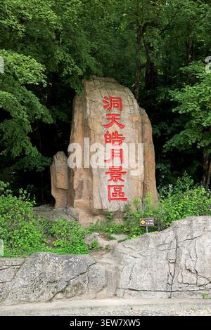 Ein massiver hellbrauner Granitfelsen markiert den Eingang zu einem Bergwald, dessen Oberfläche natürliche Risse und verwitterte Texturen aufweist. Die Vorderseite von Stockfoto