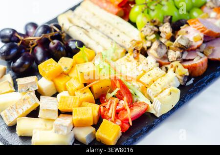 Käseplatte kunstvoll auf dunkler Steinoberfläche angeordnet. Frische Trauben, Wurstwaren und verschiedene Käsesorten sorgen für eine elegante Präsentation. Lebendige Farben und Tex Stockfoto