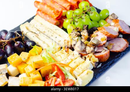 Käseplatte kunstvoll auf dunkler Steinoberfläche angeordnet. Frische Trauben, Wurstwaren und verschiedene Käsesorten sorgen für eine elegante Präsentation. Lebendige Farben und Tex Stockfoto