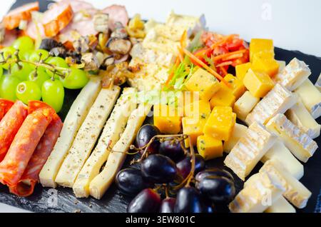 Käseplatte kunstvoll auf dunkler Steinoberfläche angeordnet. Frische Trauben, Wurstwaren und verschiedene Käsesorten sorgen für eine elegante Präsentation. Lebendige Farben und Tex Stockfoto