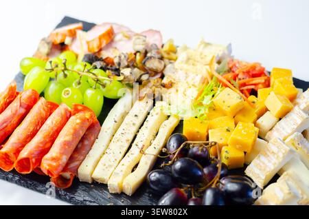 Käseplatte kunstvoll auf dunkler Steinoberfläche angeordnet. Frische Trauben, Wurstwaren und verschiedene Käsesorten sorgen für eine elegante Präsentation. Lebendige Farben und Tex Stockfoto