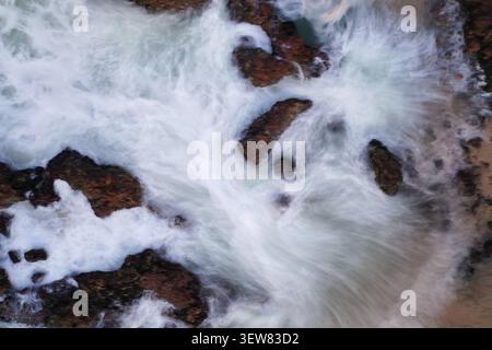 Blick aus der Vogelperspektive auf Flynns Beach mit weißem Meeresschaum, der um dunkle Felsvorsprünge entlang der Küste in Port Macquarie, New South Wales, Australien, wirbelt. Stockfoto