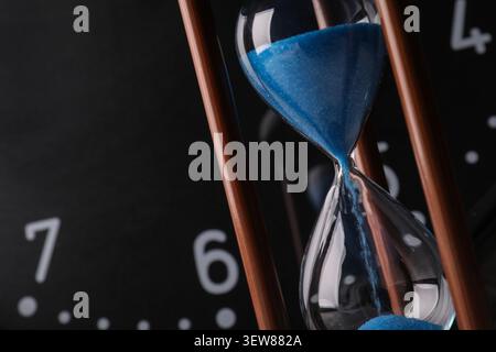 Nahaufnahme einer Sanduhr mit blauem Sand und Uhrhintergrund Stockfoto