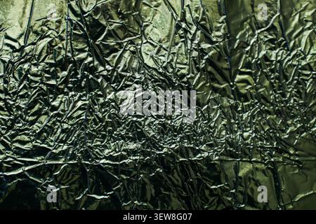 Vollformathintergrund aus gefalteter und zerknitterter dunkelgrüner Metallic-Folie mit glänzenden reflektierenden Highlights. Diese abstrakte zerknitterte Alufolie-Textur mit mir Stockfoto