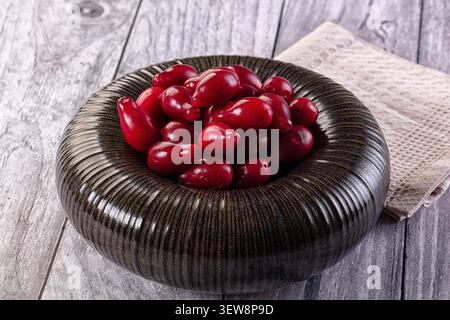 Leuchtend rote Beeren in glänzender dunkler Keramikschale mit gerippter Textur. Rustikales Holz Hintergrund neutrales Tuch schaffen warme, natürliche Komposition. Stockfoto