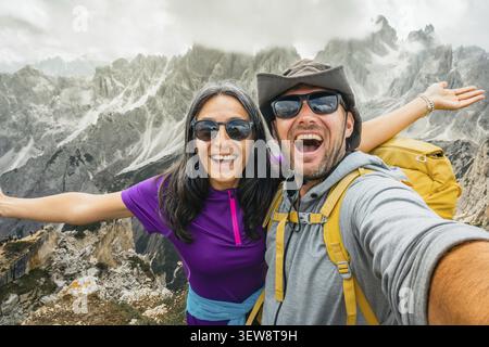 Fröhlich glückliche zwei Wanderfreunde, die Selfie am Aussichtspunkt Cadini di Misurina machen. Millennial Guy Girl genießt Sommerausflüge und lacht Stockfoto