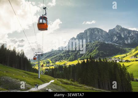 Dolomiten, Italien - 27. juli 2026: Gondelbahn Colfosco Orange über saftig grüne Almwiesen Wanderweg Tal Stadt Kiefernwald towe Stockfoto