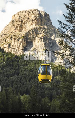 Dolomiten, Italien - 27. juli 2026: Gelbe Seilbahn Colfosco Bergbahn über saftig grüne Almwiesen Wanderweg Tal Stadt Kiefernwald towe Stockfoto
