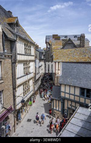 Touristen strömen durch eine mittelalterliche Gasse, umgeben von traditionellen Fachwerkhäusern innerhalb der Festungsmauern von Mont-Saint-Michel, Touristenattraktion Stockfoto