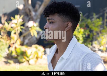 Afroamerikaner, der im Hof bei Sukkulenten schaut, mit weißem Hemd, Kopierraum Stockfoto