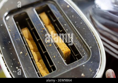 Braune Brotscheiben im Toaster aus Edelstahl, Nahaufnahme mit Krümeln und Textur, Küchengerät in Gebrauch, Vorbereitung des Frühstücks am Morgen Stockfoto