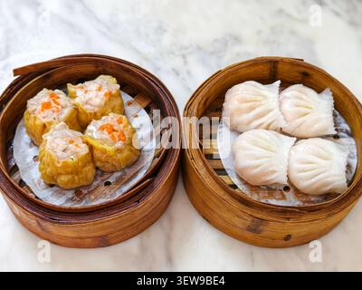 Gedämpftes Dim Sum-Sortiment mit siu mai und Garnelenknödeln, serviert in traditionellen Bambuskörben. Stockfoto