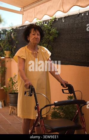 Ältere Frau mit Mobilitätsschwierigkeiten mit Rollator Walker auf einer Sonnenterrasse Stockfoto