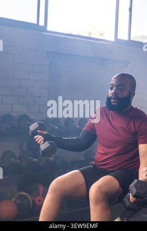 Afroamerikaner sitzen Bank mit Hexen-Kurzhanteln, strecken den linken Arm im Fitnessstudio, Kopierraum Stockfoto