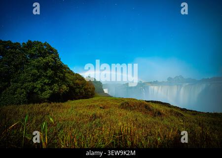 Majestätische Victoria Falls mit goldenem Sonnenuntergang und seltenem Mondbogen bei Nacht Stockfoto