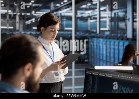 Das Engineering-Team nutzt ein digitales Tablet in einem Rechenzentrum, um KI-Virtualisierung zu verwalten und die Serverinfrastruktur zu optimieren. Stockfoto