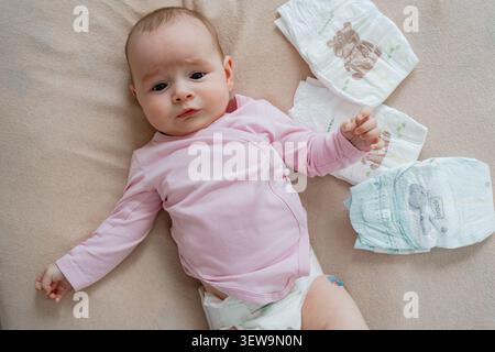 Nahaufnahme eines süßen Mädchens in rosa Kleidung, das auf einer weichen Decke liegt, umgeben von sauberen Windeln während der Morgenpflege. Entzückend Stockfoto