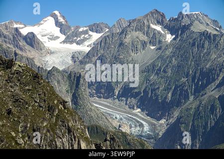 Aus der Vogelperspektive auf den Fiescher Gletscher, umgeben von zerklüfteten Berggipfeln, felsigen Hängen und schneebedeckten Gipfeln unter einem klaren blauen Himmel im Fieschertal, Vala Stockfoto