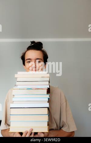 Glücklicher Teenager, der einen großen Stapel Bücher hält Stockfoto