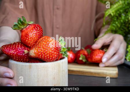 Nahaufnahme einer Frau, die eine Holzschale mit Reifen Erdbeeren in der Küche trägt. Saisonale Ernte, frische Produkte, gesunde Kochzutat und Stockfoto