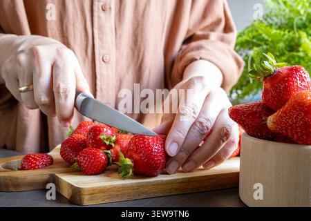 Frau, die frische Erdbeeren auf Holzbrett in der Küche schneidet. Gesunde Dessertzubereitung, saisonale Zutatenverarbeitung und hausgemachte Lebensmittel Conceep Stockfoto