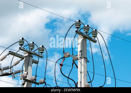 Nahaufnahme von elektrischen Isolatoren und Stromleitungen an Betonmasten. Stromverteilungsgeräte und Versorgungsmasten vor blauem Himmel. Stockfoto
