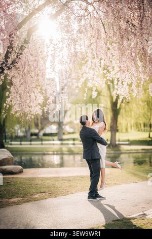 Der Mann hält die Frau unter rosa Kirschblüten Stockfoto