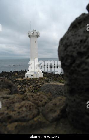 Mangru Lighthouse, eingerahmt von vulkanischen Basaltblöcken auf Udo Island, Jeju, Südkorea, mit Blick auf die felsige Küste. Stockfoto