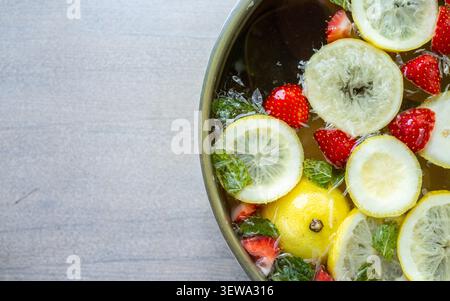 Oberansicht von Zitronenscheiben, Erdbeeren, Minzblättern und Eis, die in einer gekühlten Schale auf hellem Steinboden schweben, und schaffen eine frische bunte Essensarrangement mit erfrischender Sommergetränkezubereitungsstimmung Stockfoto