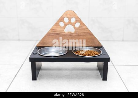 Moderne handgefertigte hölzerne erhöhte Haustier-Futterstation mit doppelten Edelstahl-Schüsseln im Pfotenabdruck-Design. Stilvolle Wohnraumdekoration für die gesunde Fütterung von Hunden und Katzen Stockfoto