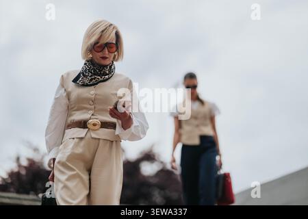 Zwei Geschäftsfrauen, die in stilvollen beigefarbenen Outfits Treppen hinuntergehen, während eine ihr Smartphone überprüft Stockfoto