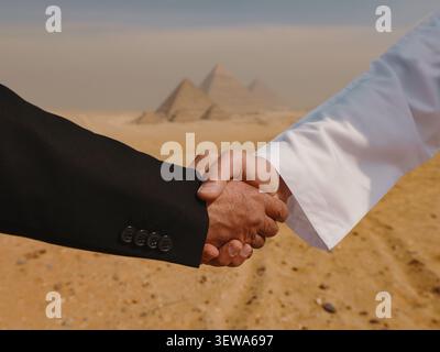 Zwischen einem westlichen Geschäftsmann in schwarzem Anzug und einem arabischen Mann in weißer Kandura, der vor den Pyramiden von Gizeh einen Deal besiegelt Stockfoto