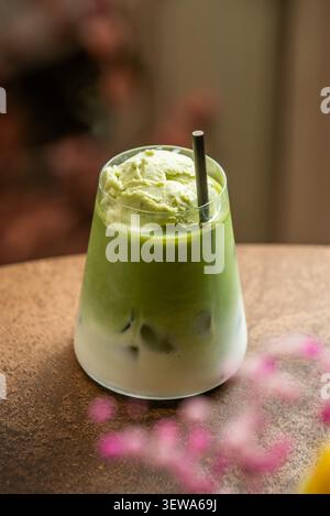Eismatcha Latte mit grünem Tee-Eis und schwarzem Strohhalm, mit rosa Blumenbokeh im Vordergrund. Stockfoto