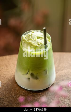 Eismatcha Latte mit grünem Tee-Eis und schwarzem Strohhalm, mit rosa Blumenbokeh im Vordergrund. Stockfoto