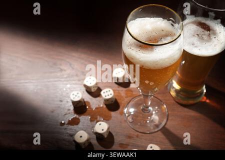 Bierglas und Spielwürfel in einer nassen dunklen Holzbar, Entspannung nach der Arbeit im Pub, Kopierraum, ausgewählter Fokus, enge Tiefe des Feldes Stockfoto
