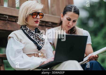 Zwei professionelle Frauen arbeiten an einem Laptop zusammen, während sie im Freien arbeiten Stockfoto