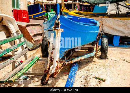 Ein leuchtend blaues Boot ruht auf einem rostigen Anhänger in Valetta, Malta. Stockfoto