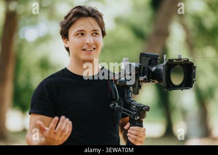 Junger Videograf, der eine professionelle Kamera auf einem Gimbal bedient, während er im Freien in einem Park filmt Stockfoto
