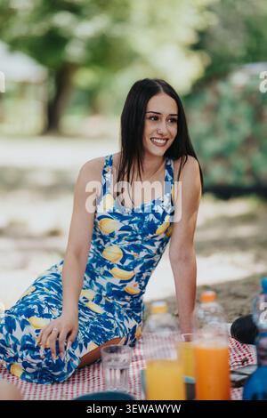 Eine junge Frau lächelt bei einem sonnigen Picknick in einem blauen Kleid mit Zitronenmuster auf einer Decke Stockfoto