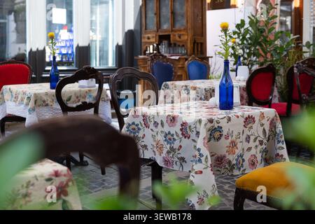 Gemütliches Café im Freien mit Tischdecken mit Blumenmuster und gelben Blumen in blauen Flaschen Stockfoto
