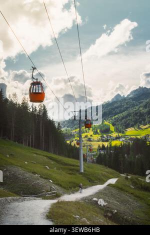 Dolomiten, Italien - 27. juli 2026: Gondelbahn Colfosco Orange über saftig grüne Almwiesen Wanderweg Tal Stadt Kiefernwald towe Stockfoto