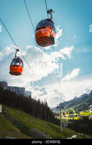 Dolomiten, Italien - 27. juli 2026: Gondelbahn Colfosco Orange über saftig grüne Almwiesen Wanderweg Tal Stadt Kiefernwald towe Stockfoto