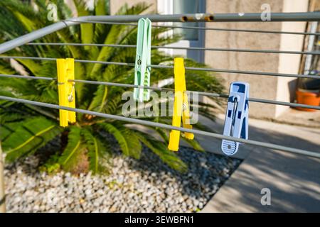 Bunte Kleiderschalen hängen an einer Metalllinie in der Nähe einer Palmenpflanze. Die Szene fängt einen sonnigen Tag mit einer sauberen Wäscherei im Freien ein. Stockfoto