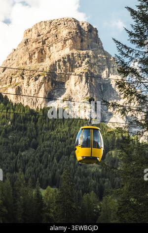 Dolomiten, Italien - 27. juli 2026: Gelbe Seilbahn Colfosco Bergbahn über saftig grüne Almwiesen Wanderweg Tal Stadt Kiefernwald towe Stockfoto
