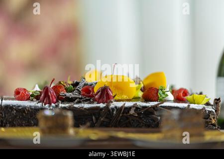 Eine Nahaufnahme eines reichhaltigen Schokoladenkuchens mit Himbeeren, Erdbeeren, Pfirsichscheiben und essbaren Blumen, die mit Puderzucker bestäubt sind Stockfoto