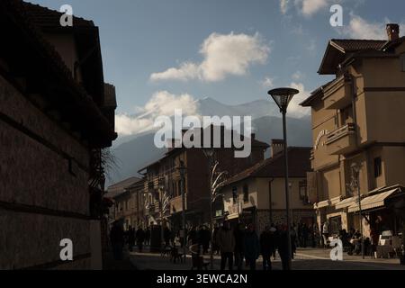 Fußgänger genießen einen frischen Tag in Bansko, Bulgarien, bei einem Spaziergang durch die traditionelle Architektur mit den majestätischen Pirinbergen darüber. Stockfoto