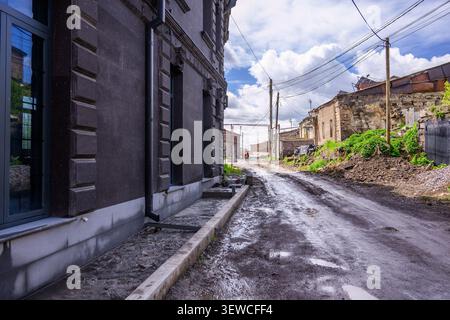 Nasse, enge Straße mit alten Gebäuden auf beiden Seiten. Der Himmel ist teilweise bewölkt mit blauen Flecken. Über die Straße erstrecken sich Freileitungen. Die Straßenoberfläche ist u Stockfoto