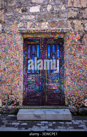 Farbenfrohe Graffiti bedecken eine Steinmauer um die Holztür. Die Tür ist mit blauen Glaspaneelen ausgestattet. Die Wand zeigt lebendige, chaotische Kunstwerke. Steintreppen führen zur Tür Stockfoto