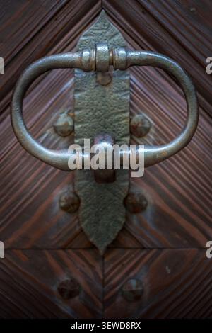 Traditioneller schmiedeeiserner Türklopfer an einer historischen Holztür mit geometrischem Holzmaserung. Stockfoto